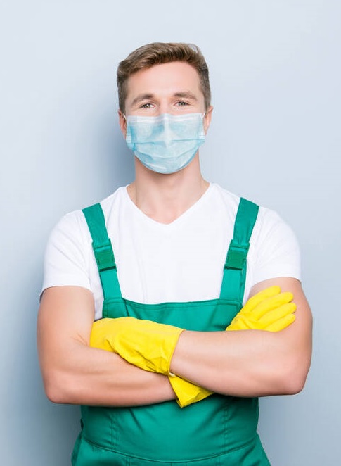 Portrait of confident janitor wearing blue face mask standing with folded arms isolated on gray background with blank space.