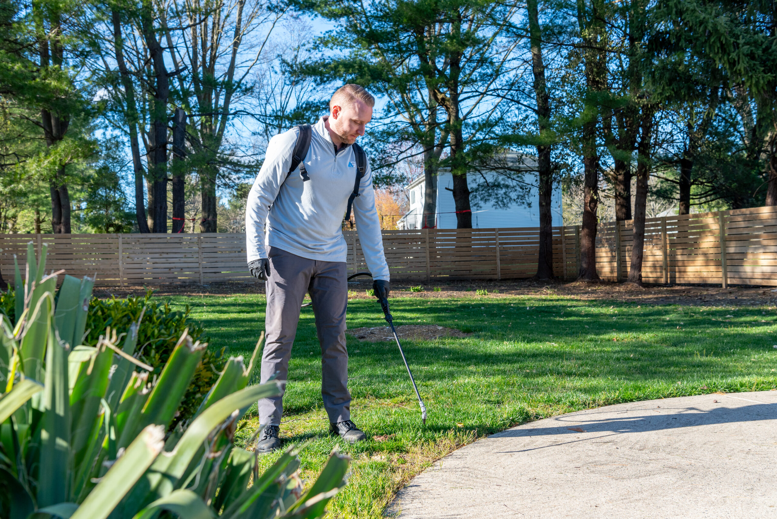 Agile Pest Control technician performing exterior ant control treatment at a residential property in Holmdel, NJ, targeting key areas around the foundation to prevent infestations.