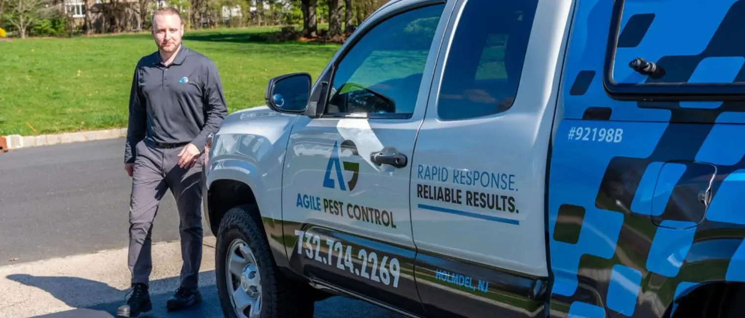 Agile Pest Control technician standing beside a branded service vehicle before performing a residential pest inspection and treatment service.